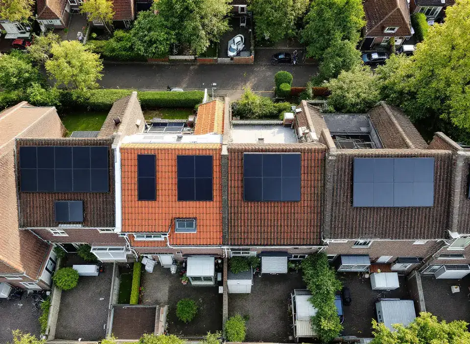 Een rij rijtjeshuizen van bovenaf gezien, met zonnepanelen op een deel van de daken en kleine achtertuinen met schuurtjes